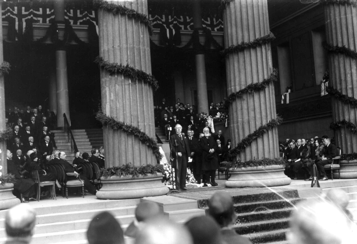 Hermann Christian Neupert, Fridtjof Nansens begravelse 17. mai 1930. Hans kiste på lit de parade i søylehallen på Universitetet, Oslo. Søylene pyntet med flagg og grønt. Æresgjester. Publikum på Universitetsplassen.