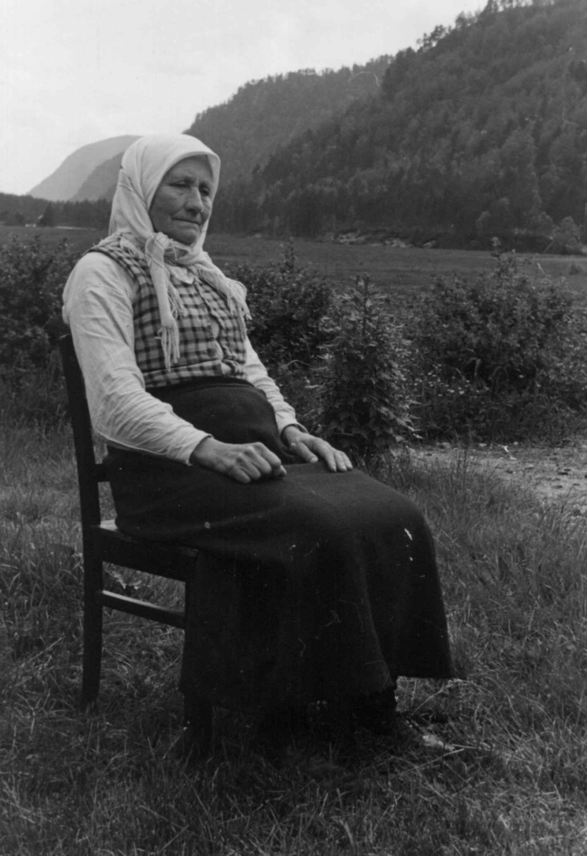 Anna Grostøl, Kari Hodne, født i bortelid 1871. Hun sitter på en stol, skogkledde fjell i bakgrunnen. Åseral 1943.
