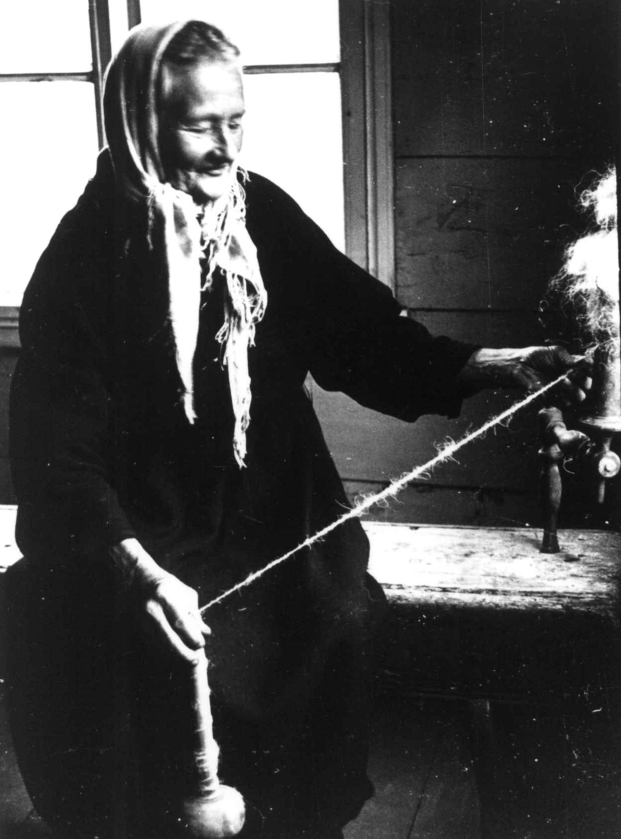 Anna Grostøl, Ragnhild Åvitsland spinner kutagl og grov ull på en liten hjemmelaget håndrokk i tre. Eiken, Hægebostad, Vest-Agder 1941.