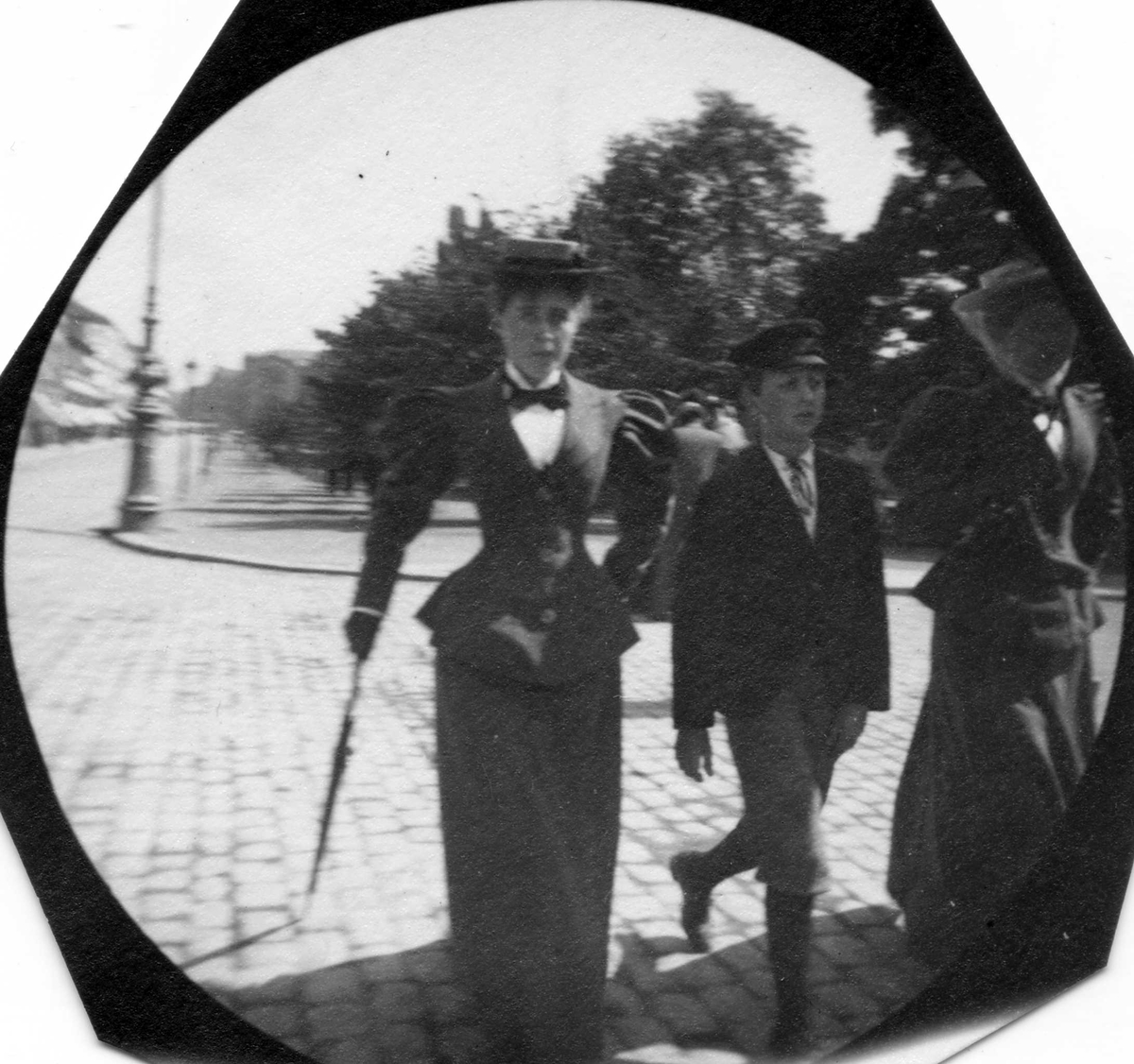 Fredrik Carl Mülertz Størmer, Frk. Sundt, en gutt og en annen kvinne spaserer langs Karl Johans gate, Oslo. Stortinget skimtes bak.