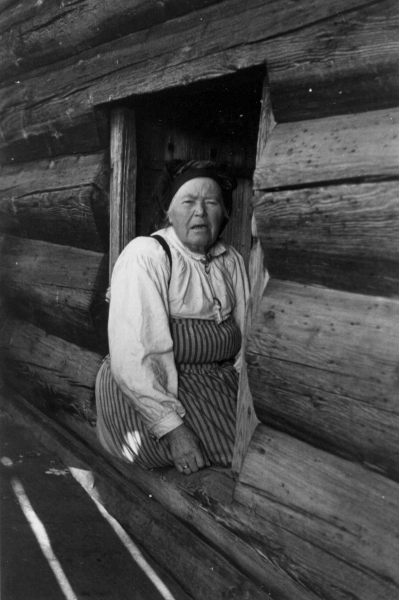 Anna Grostøl, Valle, Aust-Agder 1938. Gunnhild Viki sitter i vindusposten i et tømmerhus.