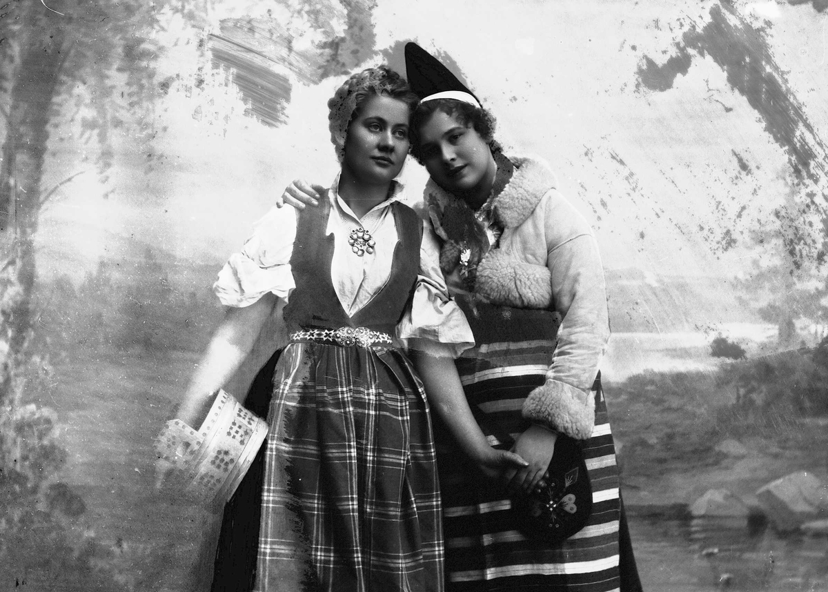 Solveig Lund, To kvinner i drakt. En holder en ambar under armen. Malt bakgrunn.