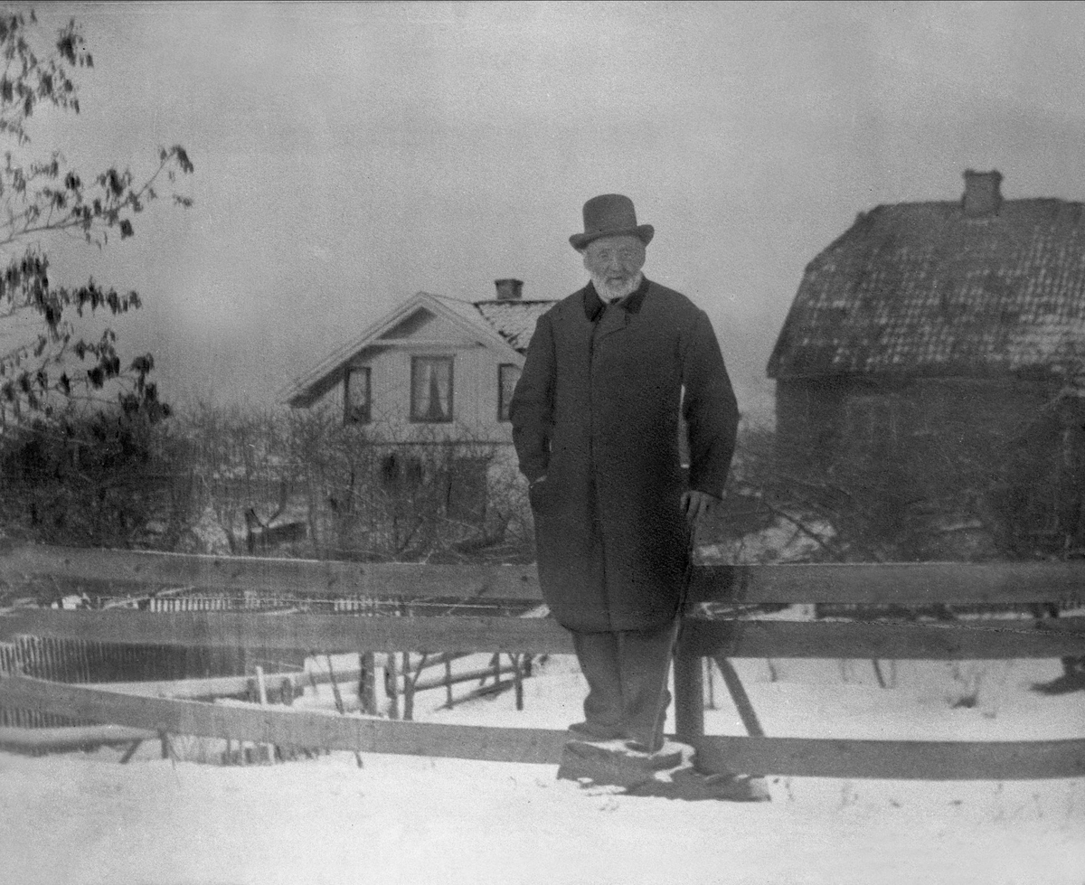 Gustav Borgen, Avfotografering. Eldre mann i yttertøy i hagen, vinter. Våningshus og uthus i bakgrunnen.
