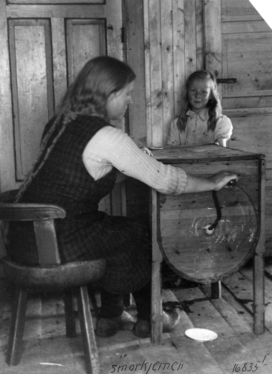 Anders Beer Wilse, En kvinne sitter ved en smørkjerne, vindekjerne, og sveiver. En jente ser på. Valle 1943.