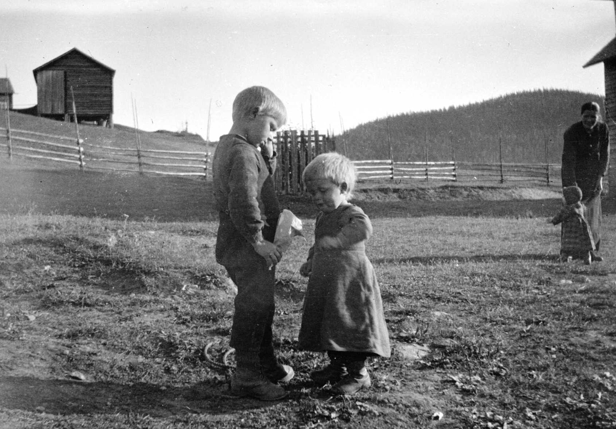 Juliane Fredrikke Langberg, Fra Eggedal, Sigdal, hos Th. Kittelsen. 2 lekende barn med tomme hesjer og uthus i bakgrunnen. Kvinne med liten jente t.h. Fra malerinne Juliane Fredrikke Langbergs (1856-1930) samling, tatt ca. 1895-1910 med motivkrets slekt og venner samt steder tilknyttet samvær med disse.