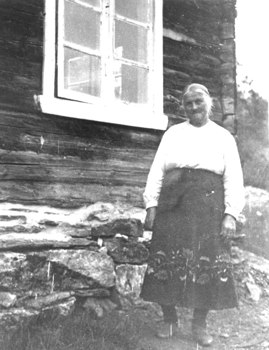 Anna Grostøl, Antagelig Lesja eller Oppdal. 1934. Kvinne står utenfor en tømmerhus med vindu.vegg