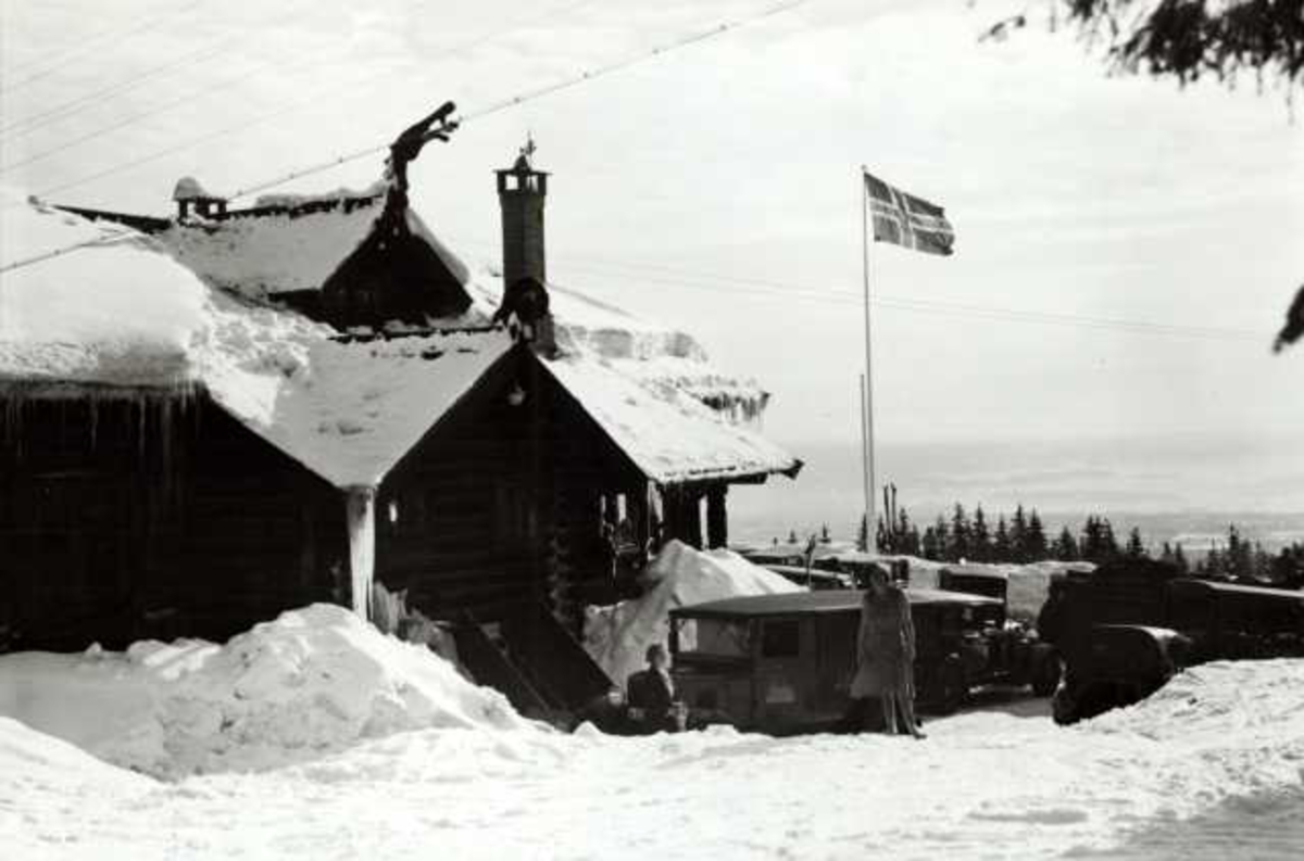 Hermann Christian Neupert, Frognerseteren Restaurant, Nordmarka, Oslo. Vintermotiv. Utsikt fra restauranten. Mennesker og biler utenfor. Flagget til topps.