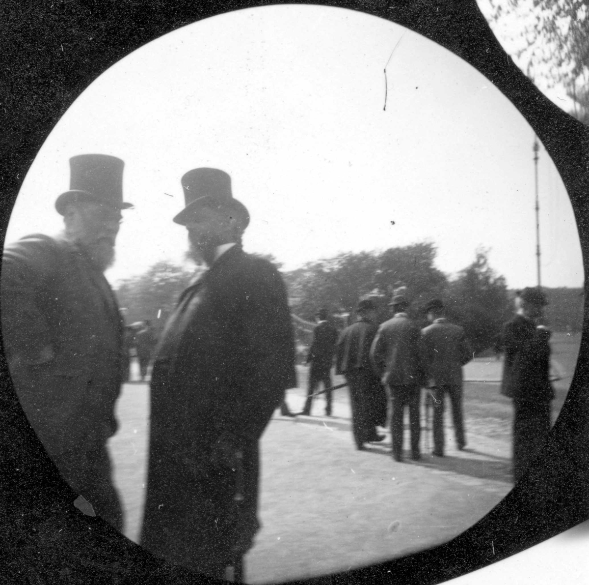 Fredrik Carl Mülertz Størmer, Stortingsmann Lund prater med en annen mann øverst på Karl Johans gate, Oslo. Slottet, Slottsparken og mennesker.