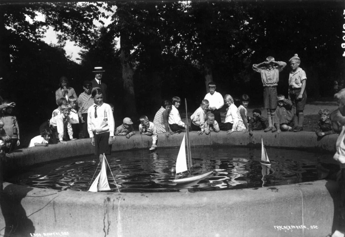 Hermann Christian Neupert, Frognerparken, Oslo. 1930-31. Lek med båt i en fontene. Barn i og rundt fontenen. Voksne i bakgrunnnen.