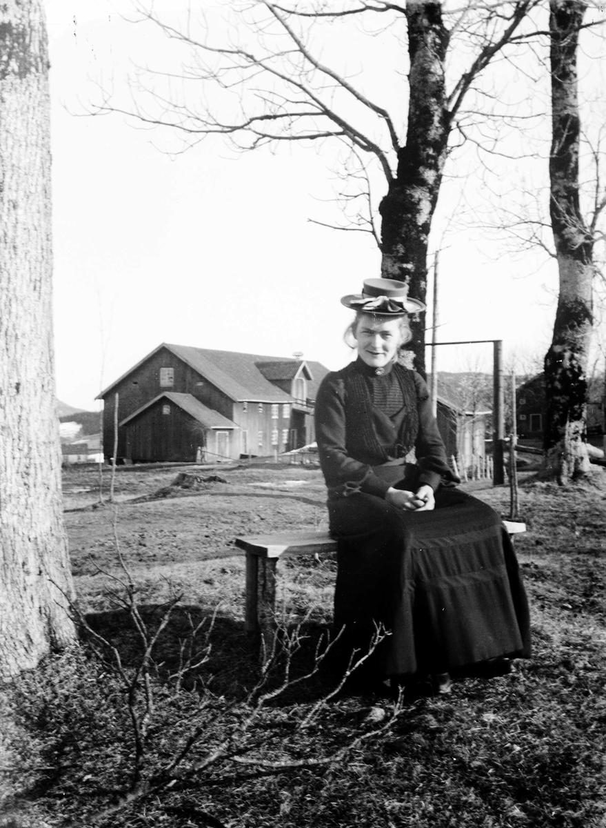 Juliane Fredrikke Langberg, Portrett av kvinne foran Hurum prestegård.Hun sitter på en benk og er kledd i fotsid kjole og hatt. Ant. fru Bull, gift med Jacob B. Bull. Fra malerinne Juliane Fredrikke Langbergs (1856-1930) samling, tatt ca.1895-1910 med motivkrets slekt og venner samt steder tilknyttet samvær med disse.