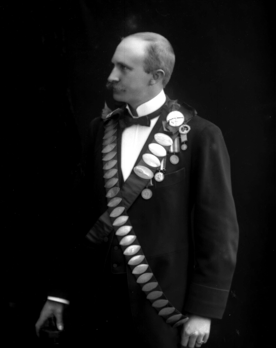 Gustav Borgen, Portrett, mann med bånd med premieplaketter, skyting. Kongebeltene til Skydeselskapet Skarpskytten. Ingeniør P Olsen, vinner i 1904(?).