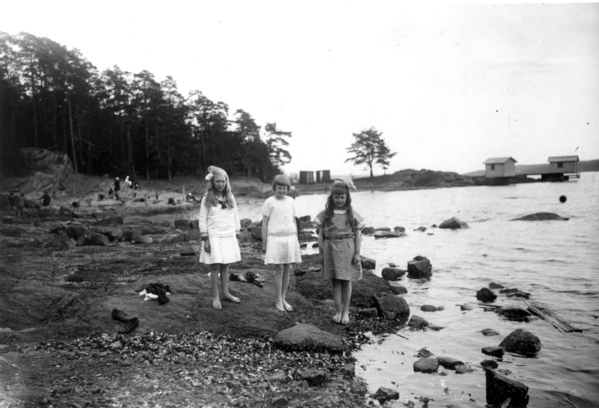 Hermann Christian Neupert, Barn i sommerkjoler i Paradisbukta på Bygdøy i Oslo i 1924. Barbeinte jenter i strandkanten. Badehusene bak tilhørte Villa Victoria