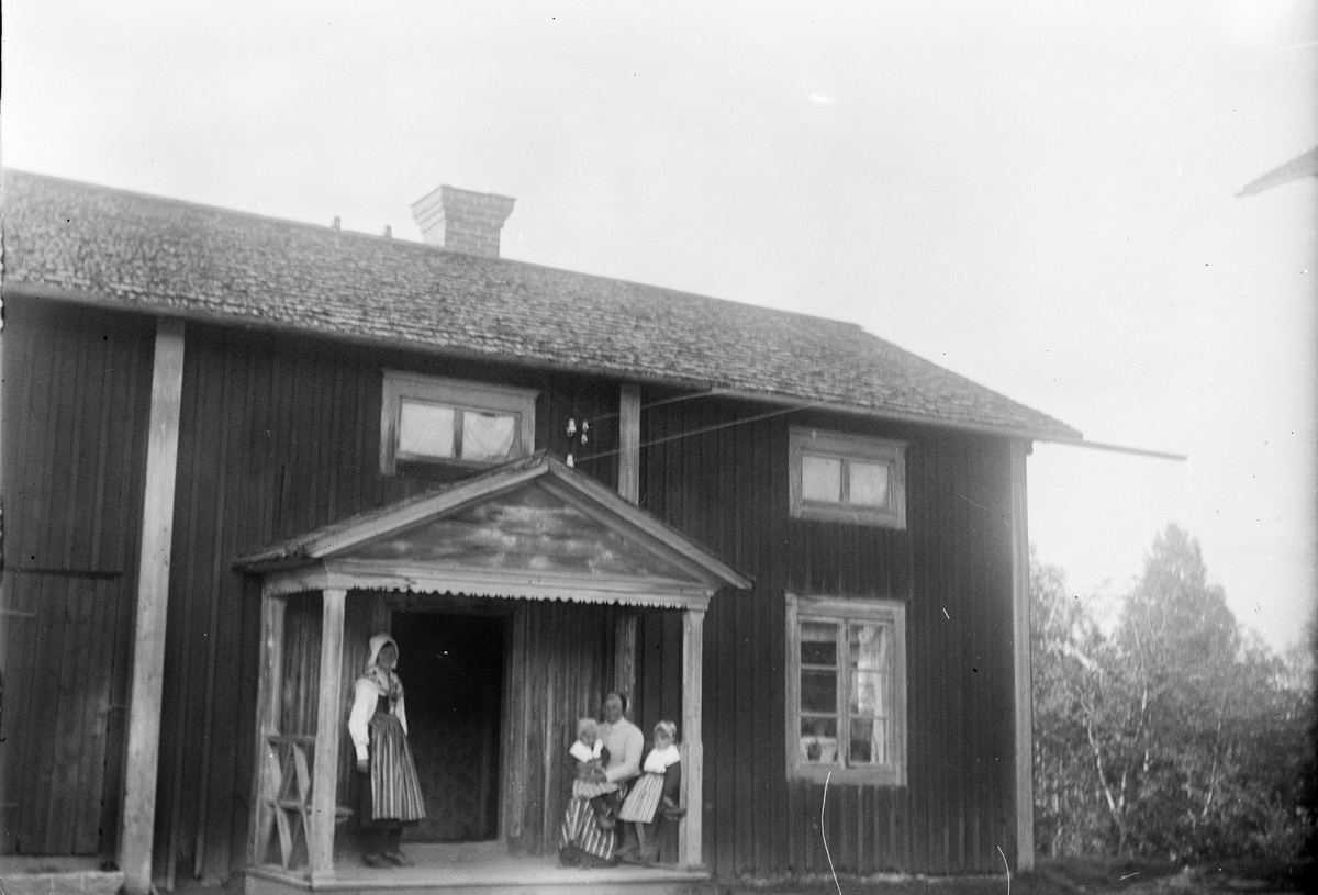 Okänd,, Two women and two little girls dressed up folk costume in front of residential buildings, probably Dalarna
