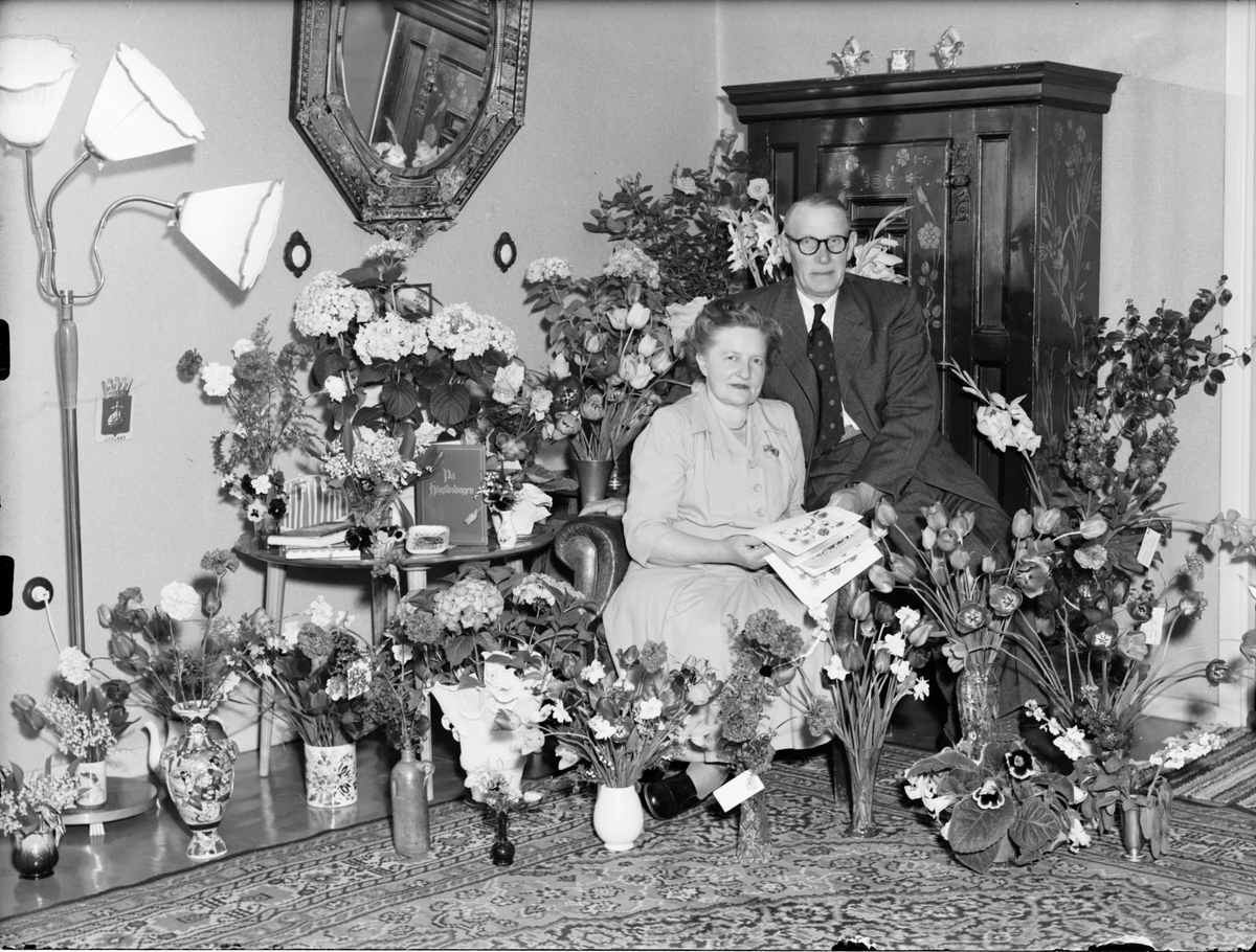 Skötsner-Edhlund, Man och kvinna i hemmiljö omgiven av blommor, Östhammar, Uppland,