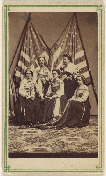 Unknown, [Five women, two standing, three seated, in costume, posed in front of two American flags]