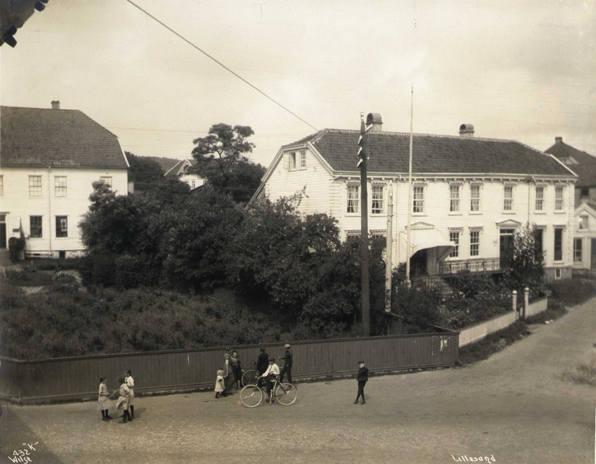 Anders Beer Wilse, Gateparti med trebygninger, Lillesand, Aust-Agder. Barn leker i forgrunnen. Huset til høyre er Carl Knudsen-gården, til venstre ligger Henschien-gården (senere rådhus).