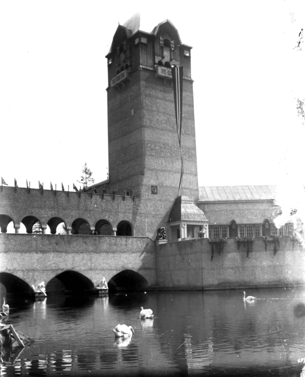 Hermann Christian Neupert, Jubileumsutstillingen på Frogner, Oslo, 1914. Festbygningen. Norsk vimpel og flagg. Vanndam med svømmede svaner i forgrunnen.