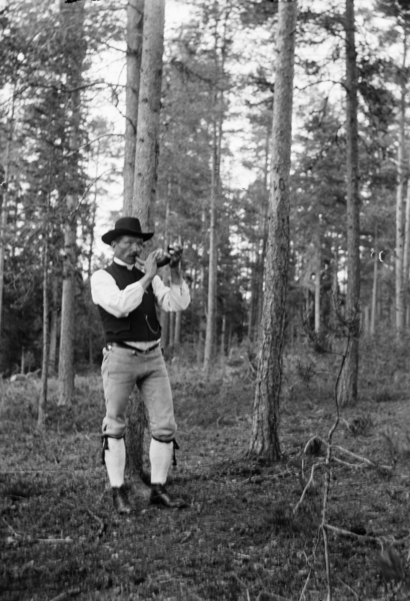 Okänd,, Man, dressed in folk costume, blows the ramhorn in the forest, probably in Sweden