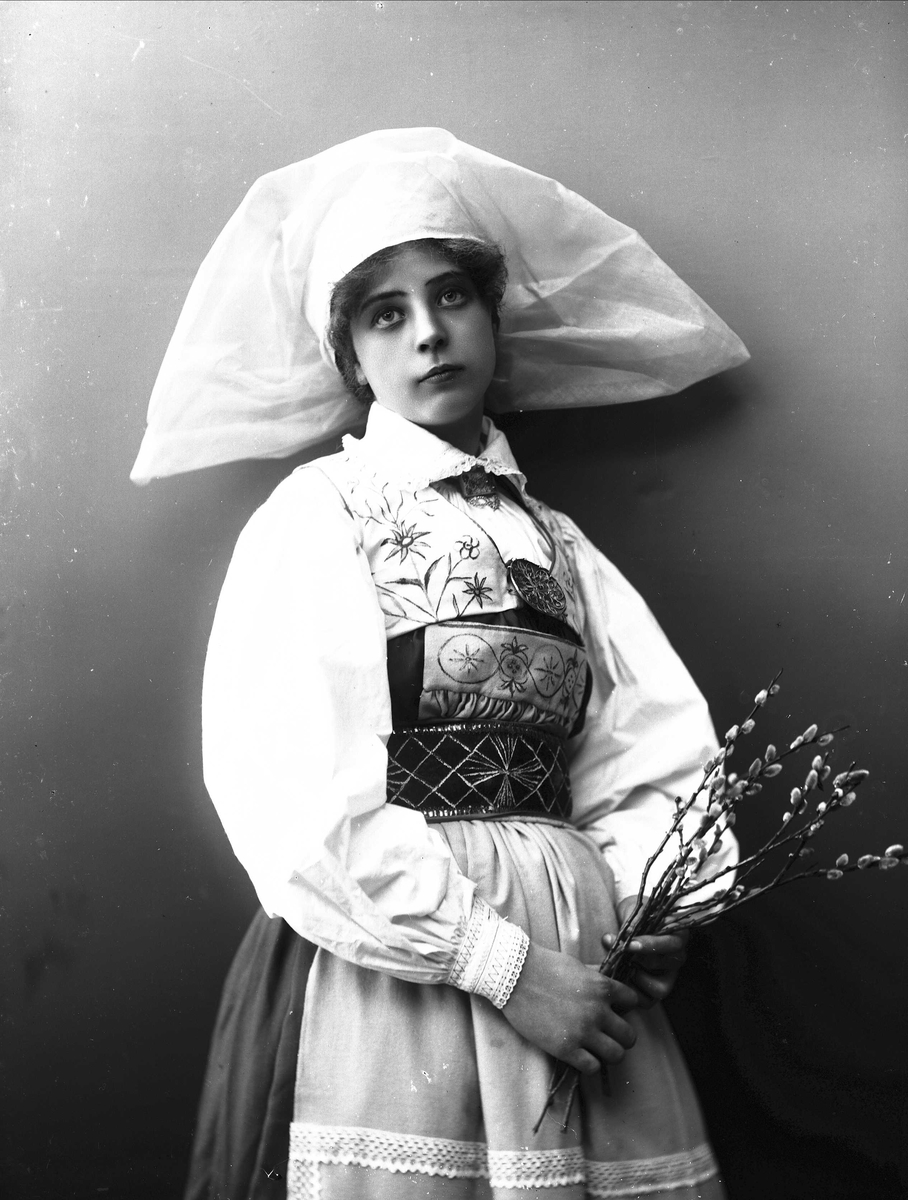 Solveig Lund, 3/4 del studioportrett av kvinne i drakt og skaut/hatt. I hendene holder hun en neve med gåsunger. Hun ser ut av fotografiet. Nøytral bakgrunn.