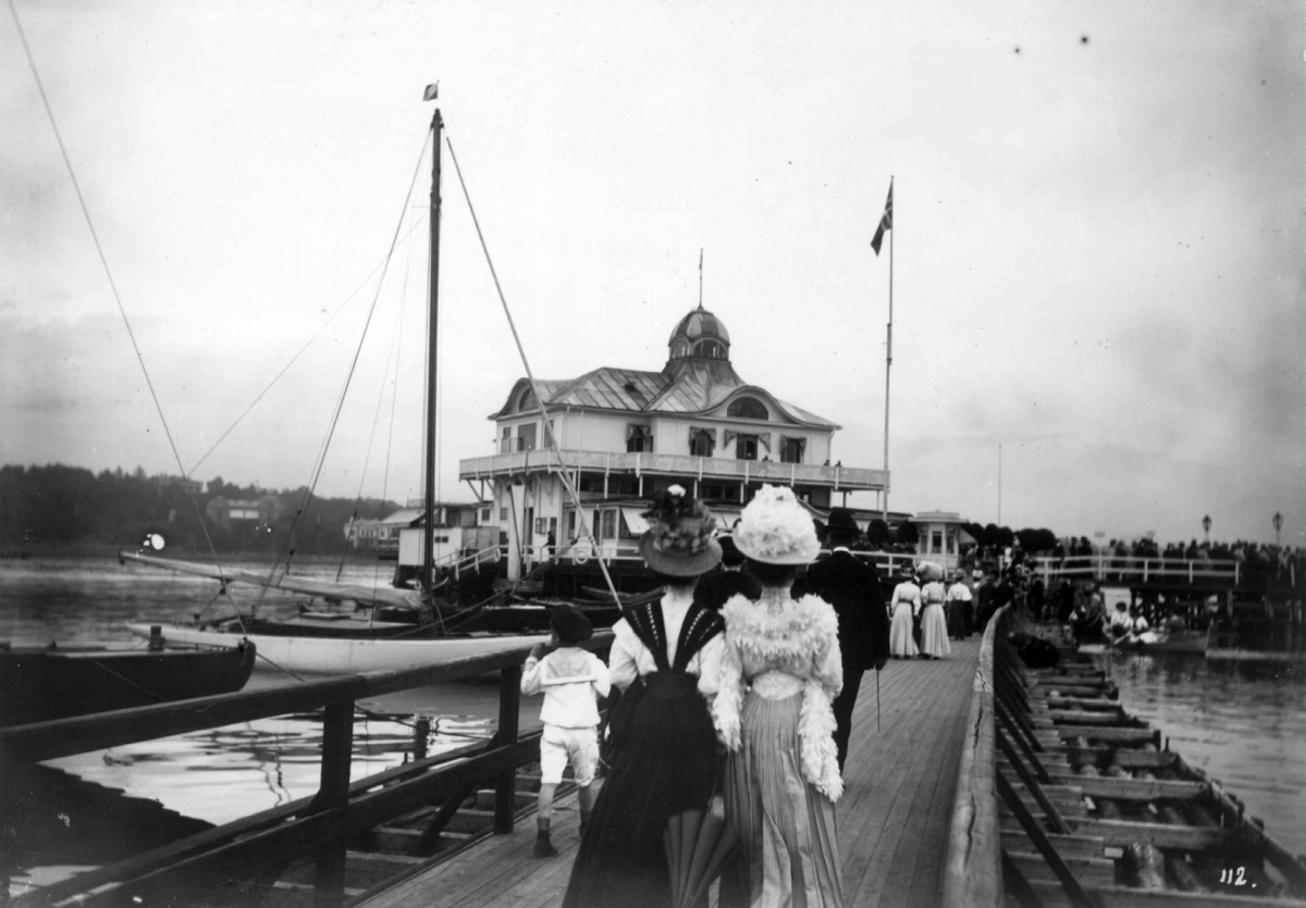 Hermann Christian Neupert, Bygdøy, Oslo 1908. Dronningen restaurant. Mennesker på brua til Dronningen. Kvinner i lange kjoler og med hatter.