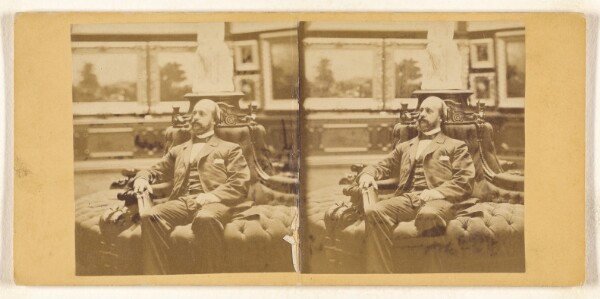 Unknown, [Close-up of bearded, bald gentleman seated on circular couch in his private art gallery, holding a carte-de-visite album]