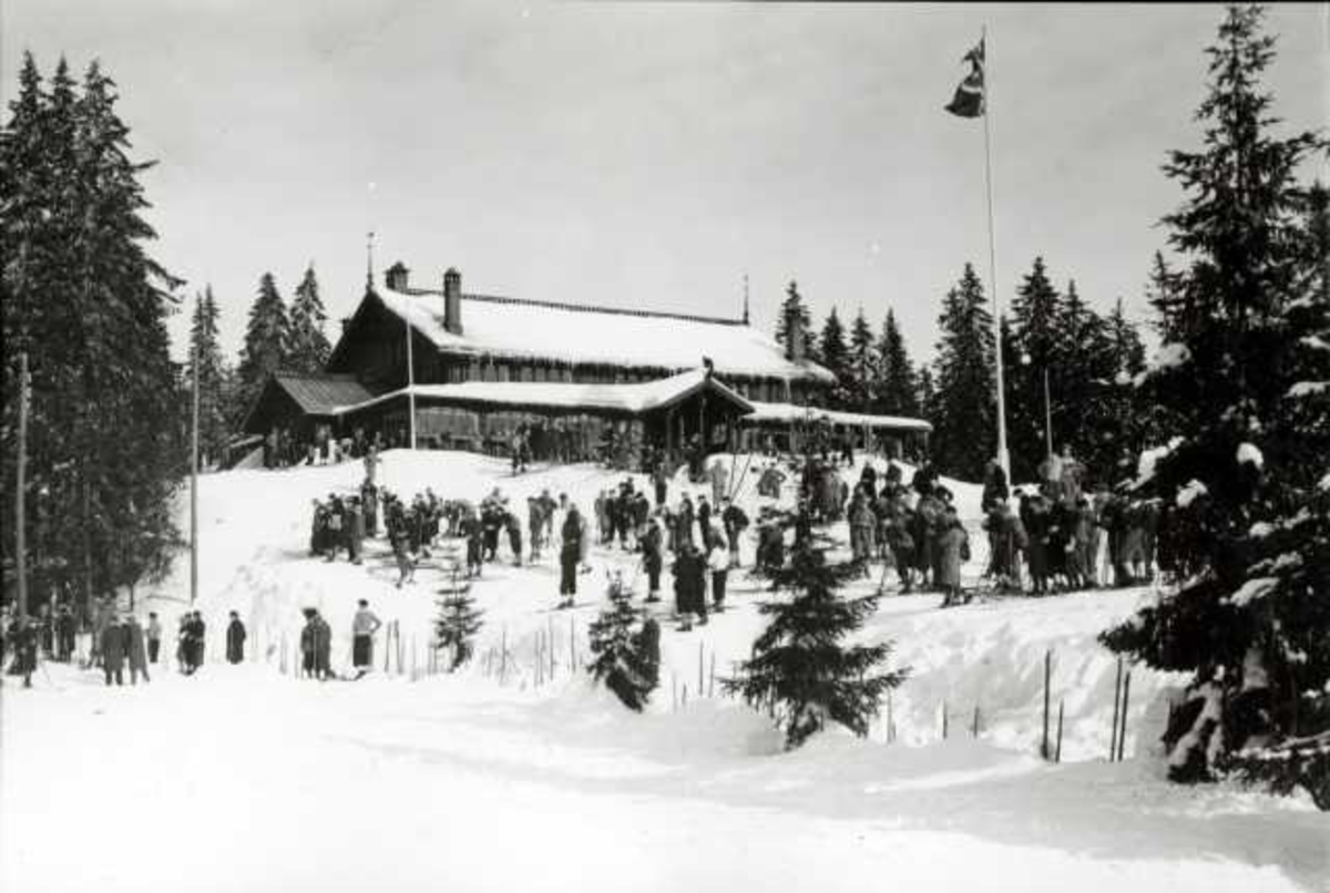 Hermann Christian Neupert, Frognerseteren Restaurant, Nordmarka, Oslo. Vintermotiv. Skiløpere utenfor restauranten. Flaggstang med flagg.