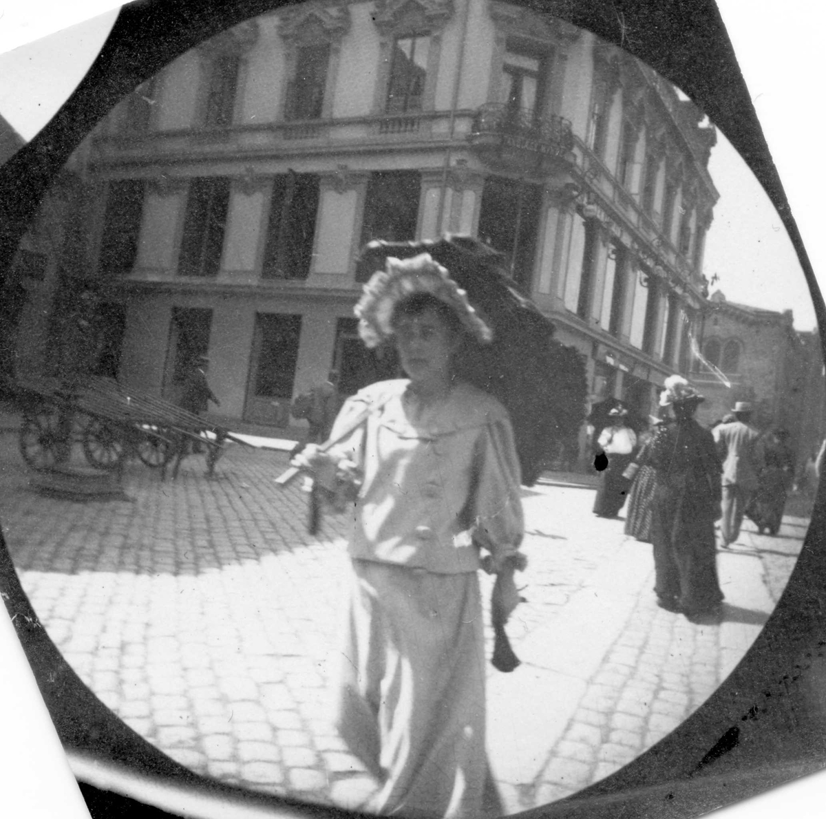 Fredrik Carl Mülertz Størmer, Mennesker spaserer langs Egertorget. Lyskledd kvinne fremst i bildet, håndkjærrer parkert.