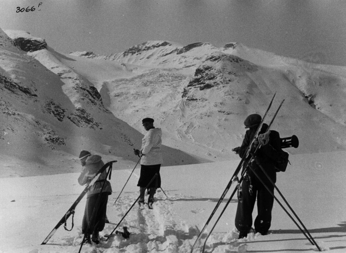 Anders Beer Wilse, Skiløpere ved Galdhøpiggen i Jotunheimen med snødekte fjell og sol.