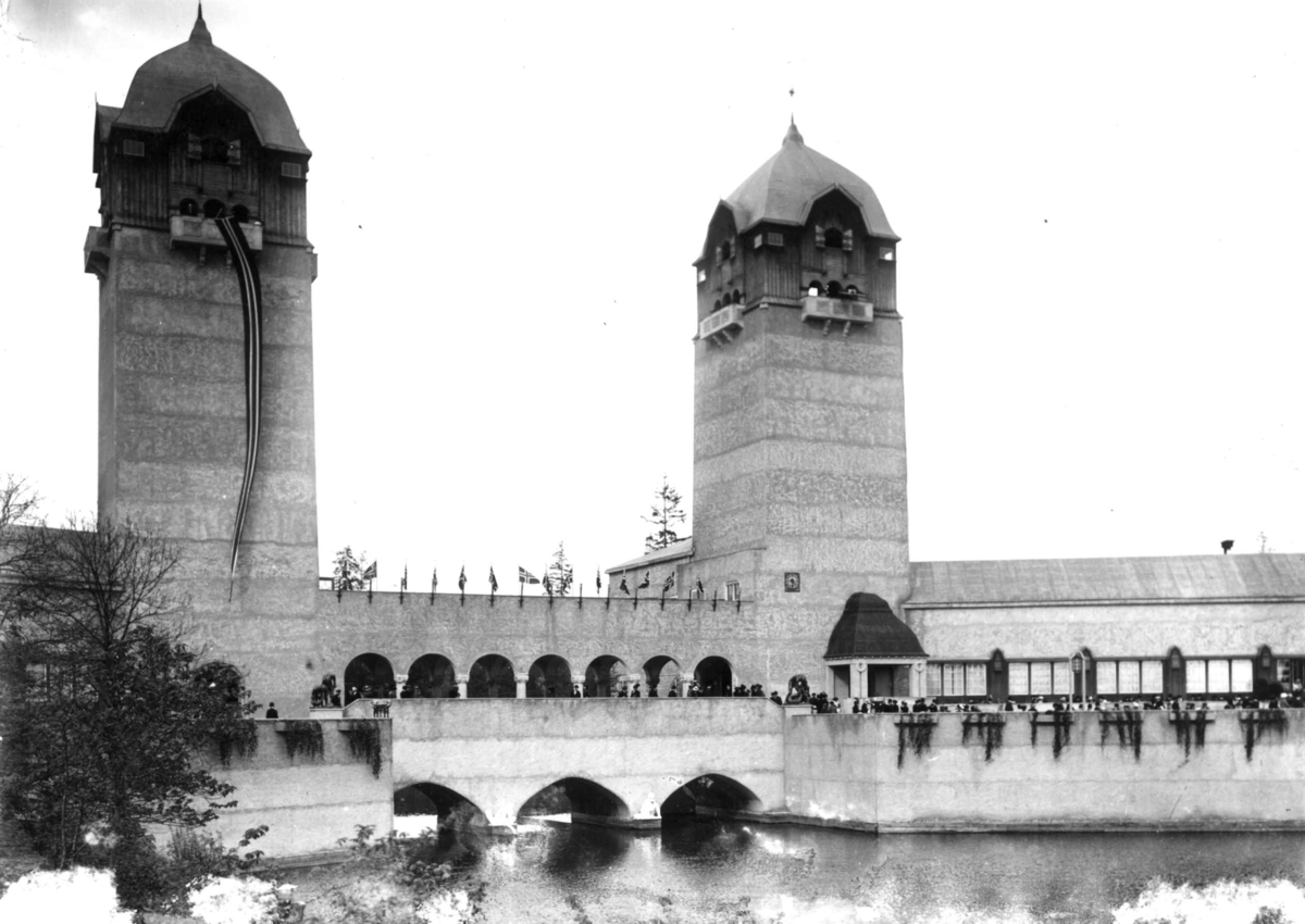 Hermann Christian Neupert, Jubileumsutstillingen på Frogner, Oslo, 1914. Festbygning og industribygning. Publikum spaserer på broene. Dam i forgrunnen.