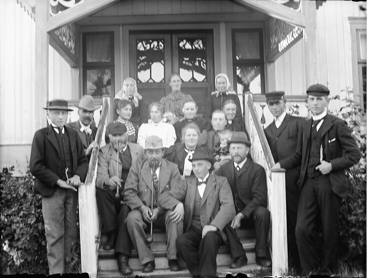 Ole Hansen Løken, GRUPPE MENN OG KVINNER PÅ VERANDA LØKEN VESTRE på Rudshøgda i Ringsaker. F. V SITTENDE I TRAPPA MED LANGPIPER OLE BOLSTAD OG LARS TOKSTAD. T. H. STÅENDE LARS STORLIEN OG OLE STORLIEN, SITTTENDE BAKERST I TRAPPA F. V. MARTHE LØKEN, MATHEA LØKEN OG KIRSTI LØKEN ( BOLSTAD ).