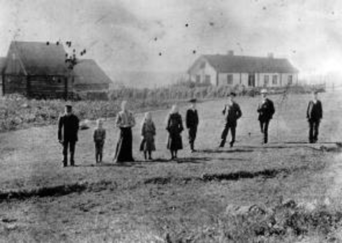 Anno Domkirkeodden, Gruppe personer foran bygninger på Maurud nedre, Helgøya. Lars Larsen Lier (1832-1910), Ottar f.1899, Teoline Torsdatter Fjeld (1853-1929) , Karen Sofie f.1895, Lovise f.1893, Torstein (1888-1971), Leonard (1885-1978), Torolf Hansen Vien f.1879, Magne (1891-1972).