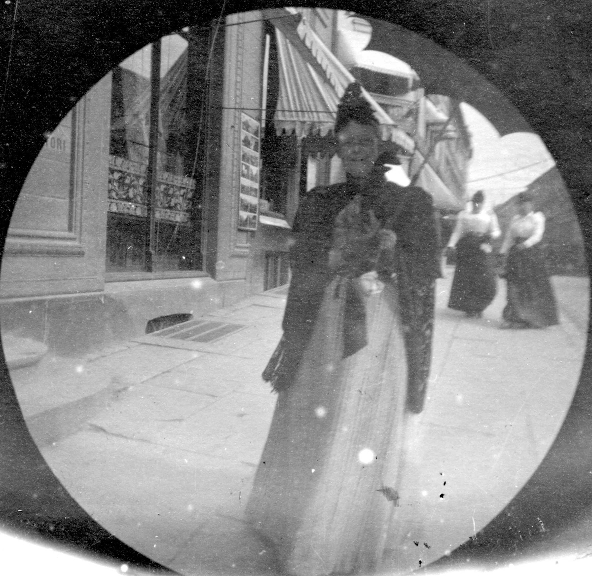 Fredrik Carl Mülertz Størmer, Fotografens mor, fru apoteker Størmer, spaserer på fortau ved butikker, Oslo.