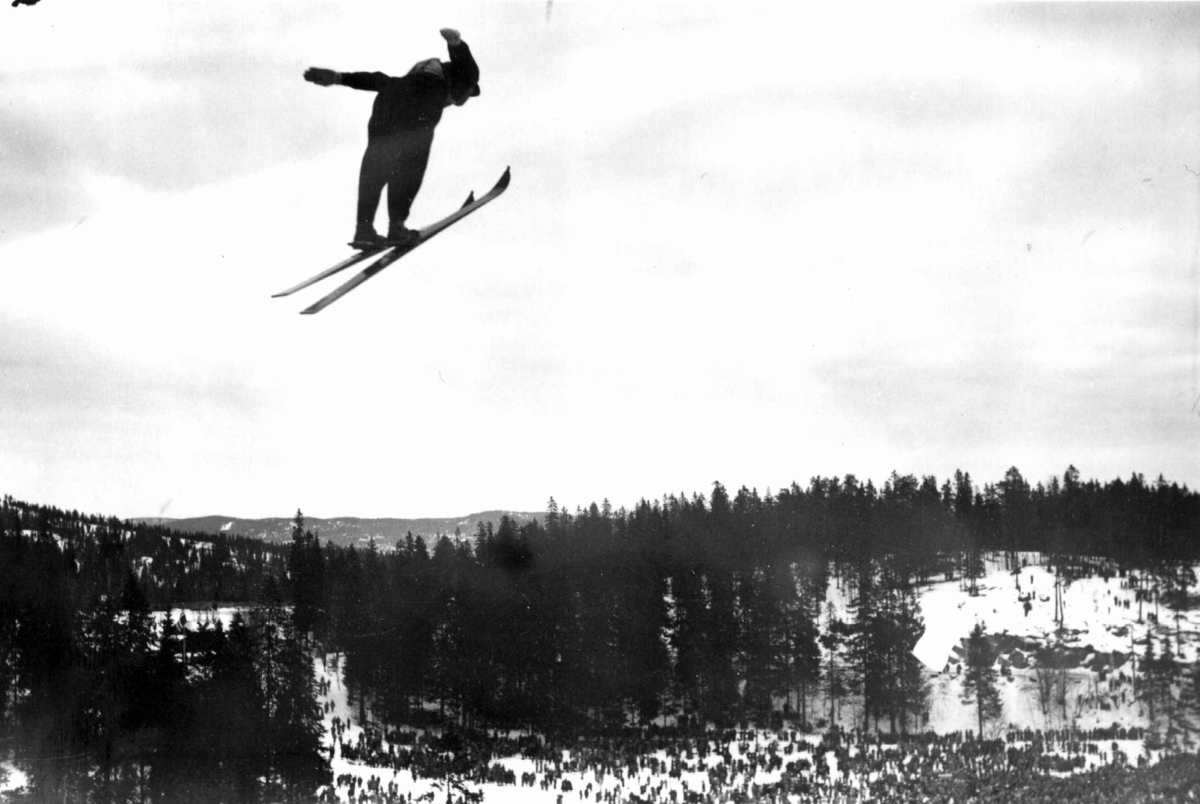 Hermann Christian Neupert, Ski. Hopprenn. Holmenkollen, Oslo 1934. Hopper i svevet. Publikum og Nordmarka ses i bakgrunnen.