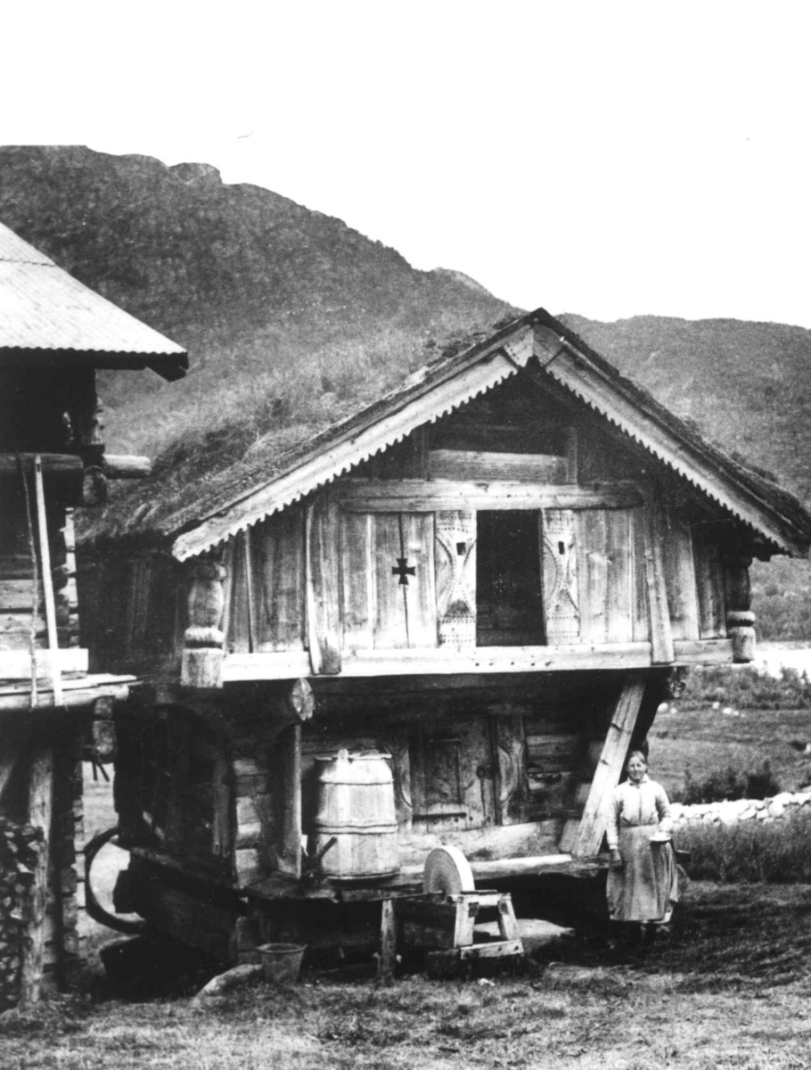 Anna Grostøl, Loft, stabbur med torvtak, en kvinne står utenfor. Ukjent sted 1935.