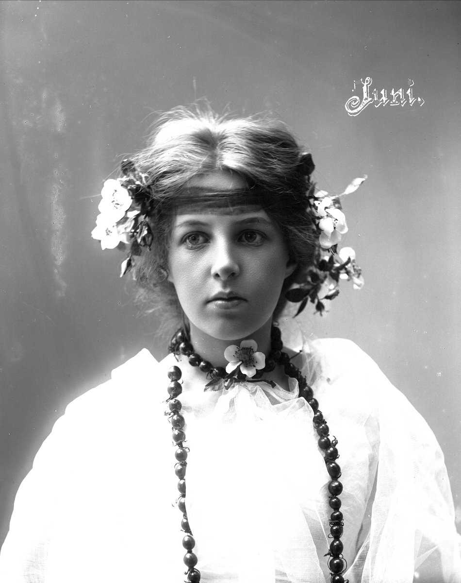 Solveig Lund, Studioportrett av kvinne i drakt med blomster i håret og halssmykke.