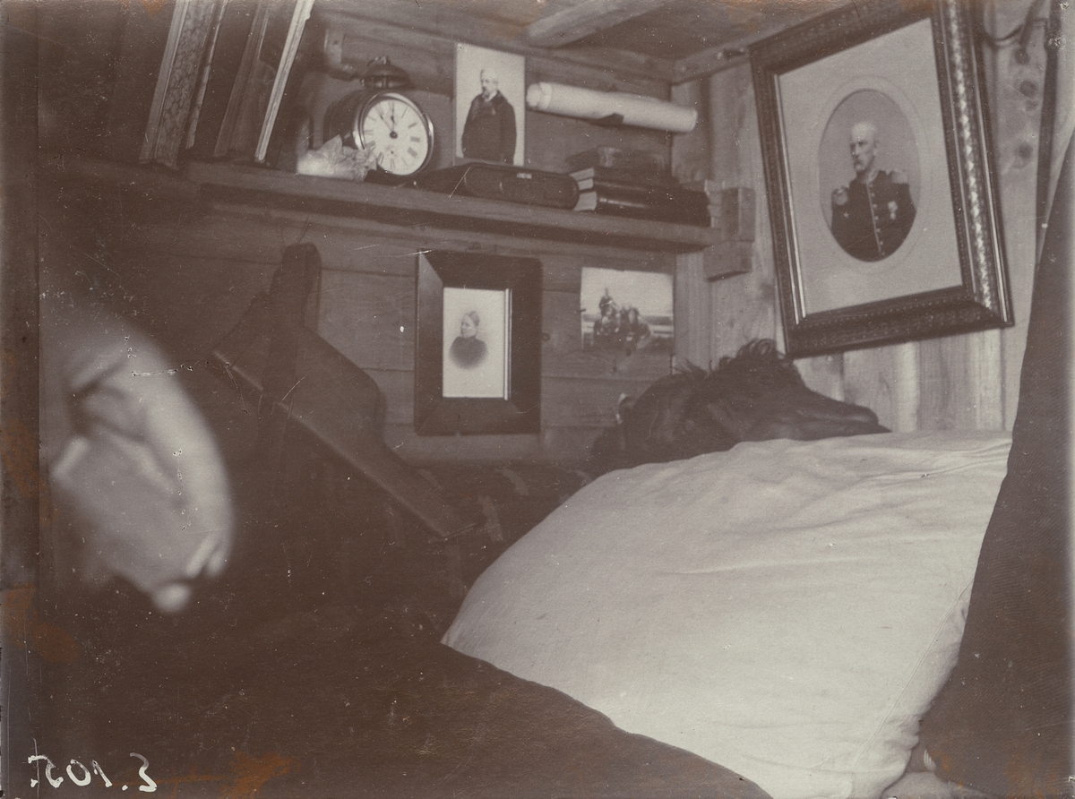 Unknown artist, Fotografi från första svenska Antarktisexpeditionen 1901-1904. Interiörbild från sovplats i ett litet trähus. På väggarna hänger tavlor och på en hylla står böcker och en väckarklocka.