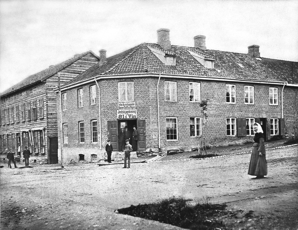 Anno Domkirkeodden, FOLK FORAN JØNSRUDGÅRDEN VED STORTORGET i Hamar, TORGGATA - KIRKEGATA, JOHN KRISTIANSENS SPISE, KAFE, THE M. M. INDSKJÆNKING AF ØL & VIN, ALKOHOL. Gården ble satt opp i 1852 og revet i 1962. Her holdt den store industriutstillingen for Hamar i 1880 holdt til.