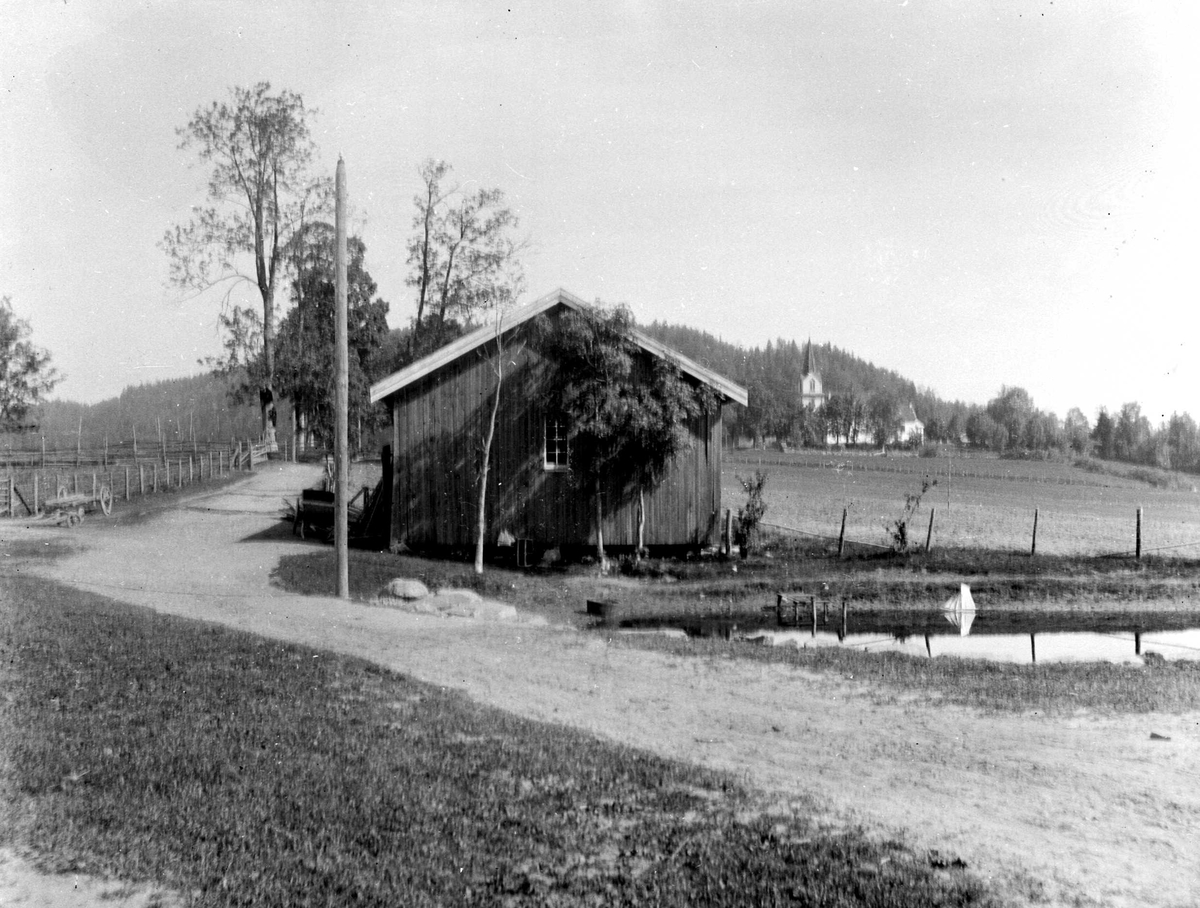 Juliane Fredrikke Langberg, Fra Hurum prestegård med Hurum kirke i bakgrunnen. Del av gårdstun med vanningsplass og inngjerdet beiteområde i bakgrunnen. Fra malerinne Juliane Fredrikke Langbergs (1856-1930) samling, tatt ca.1895-1910 med motivkrets slekt og venner samt steder tilknyttet samvær med disse.