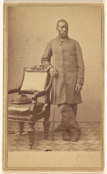 Alexander Gardner, [Black soldier standing near chair with hat in seat]