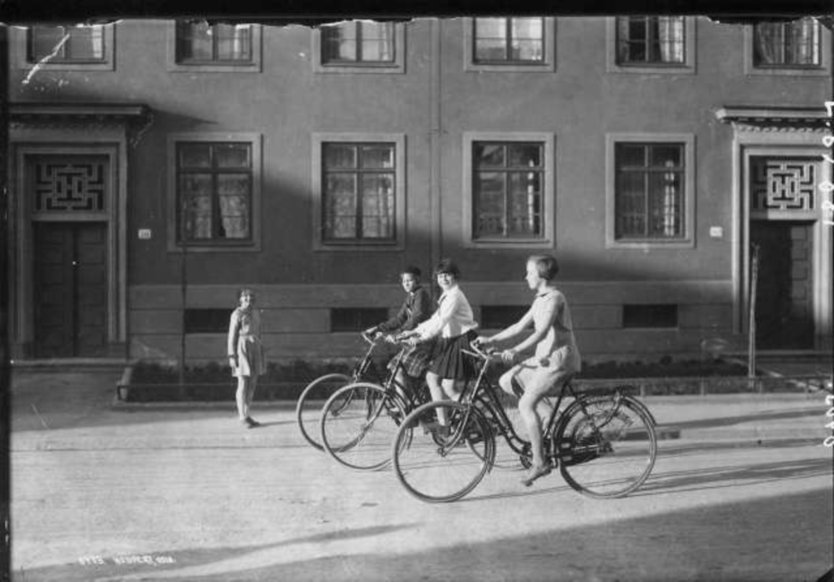 Hermann Christian Neupert, Jenter på sykkel i en bygate ant. i Oslo. Bolighus i bakgrunnen.