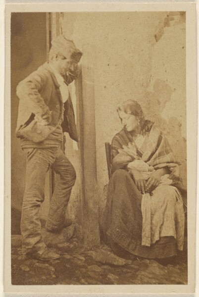 Unknown, [Man with round cap standing next to a seated woman with baby]