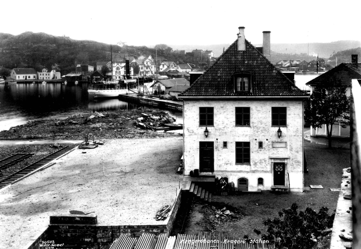 Anders Beer Wilse, Jernbanestasjon, Kragerø, Telemark. Kragerøbanen, 1927. Ved havn med skip og bybebyggelse i bakgrunnen.