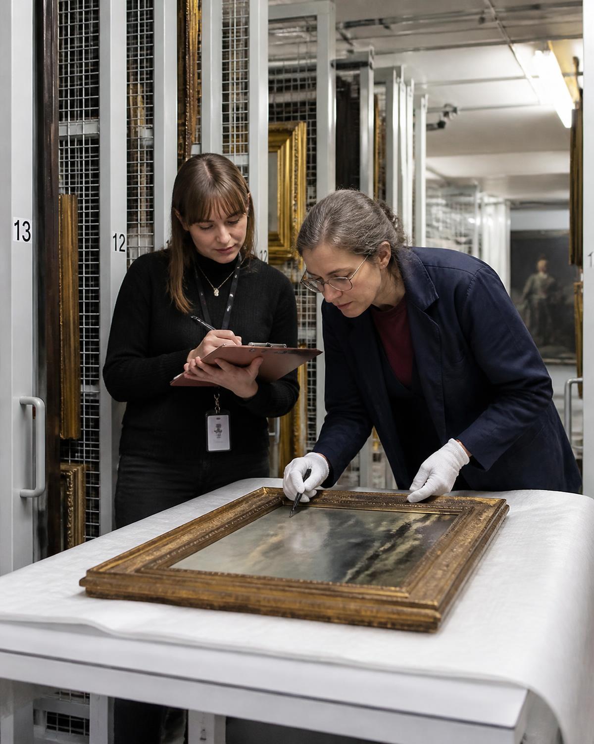 A registrar and conservator examining a framed painting in a museum storage depot